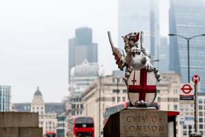een drakenbeeldhouwwerk met het wapen van de stad van londen bij de london bridge. wazig wolkenkrabbers en rode dubbeldekkers op de achtergrond. foto