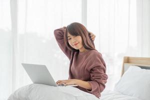 Aziatische vrouw die met laptop op bed thuis werkt at foto