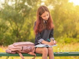 meisje tiener schoolmeisje schrijft in een notitieblok zittend op een bankje.