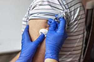 een arts vaccineert een man tegen het coronavirus in een kliniek. detailopname. het concept van vaccinatie, immunisatie, preventie tegen covid-19.