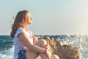 een jonge vrouw zit aan de kust van de Middellandse Zee bij zonsondergang