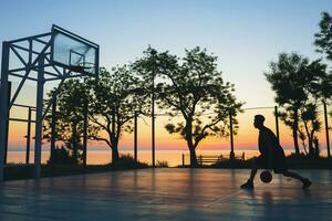 zwart Mens aan het doen sport, spelen basketbal Aan zonsopkomst, silhouet foto