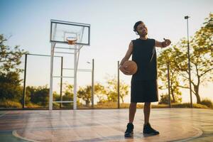 zwart Mens aan het doen sport, spelen basketbal Aan zonsopkomst, actief levensstijl, zonnig zomer ochtend- foto