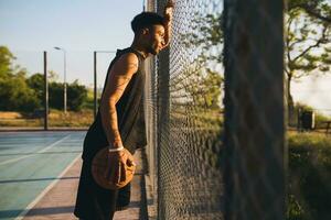 zwart Mens aan het doen sport, spelen basketbal Aan zonsopkomst, actief levensstijl, zonnig zomer ochtend- foto