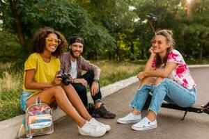 gelukkig jong bedrijf van glimlachen vrienden zittend in park Aan gras met elektrisch trap scooter foto