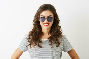 detailopname portret van aantrekkelijk jong vrouw met gekruld haar- glimlachen geïsoleerd Aan wit achtergrond vervelend zonnebril gekleed in t-shirt foto