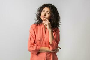 portret van jong attent brunette vrouw in oranje shirt, gekruld haar, zomer stijl, gefrustreerd gezicht uitdrukking, verdrietig emotie, op zoek terzijde, denken, probleem, idee, gemengd ras, geïsoleerd foto