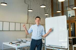 zelfverzekerd jong knap glimlachen Mens staand Bij leeg wit bord met markeerstift foto