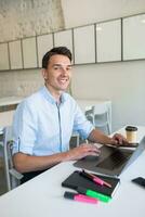 jong knap glimlachen Mens zittend in Open ruimte kantoor werken Aan laptop foto