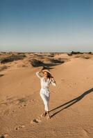 elegant mooi zorgeloos gelukkig vrouw wandelen in woestijn zand gekleed in wit kleding foto