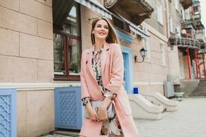 portret van aantrekkelijk elegant glimlachen vrouw wandelen stad straat in roze jas foto