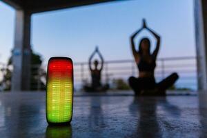 draadloze spreker Aan voorgrond van bedrijf van vrienden aan het doen yoga luisteren naar muziek- in schemer foto