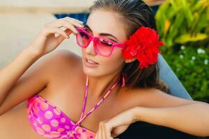 sexy vrouw Aan zomer vakantie hebben pret Bij zwembad vervelend bikini en roze zonnebril foto