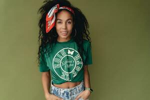 aantrekkelijk zwart Afrikaanse Amerikaans vrouw poseren in elegant hipster kleding Aan groen achtergrond foto