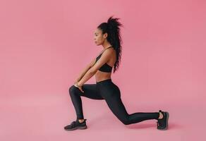 aantrekkelijk zwart Afrikaanse Amerikaans vrouw in zwart leggins geschiktheid kleding Aan roze achtergrond foto