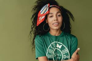 aantrekkelijk zwart Afrikaanse Amerikaans vrouw poseren in elegant hipster kleding Aan groen achtergrond foto
