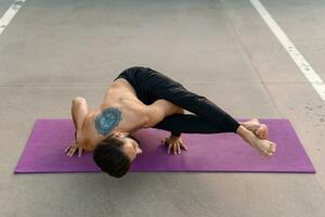 aantrekkelijk knap Mens met atletisch sterk lichaam aan het doen ochtend- yoga asana buitenshuis foto