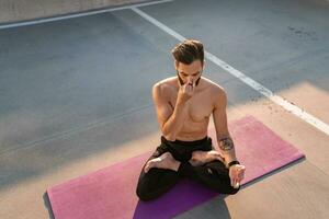 aantrekkelijk knap Mens met atletisch sterk lichaam aan het doen ochtend- yoga dzen meditatie foto