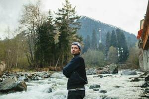 jong hipster Mens wandelen Aan een rots Bij rivier- in winter Woud foto