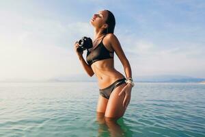 mooi vrouw, gebruind huid, zwart bikini zwempak, staand in blauw water foto