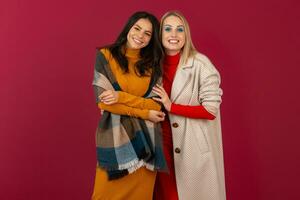 twee glimlachen aantrekkelijk elegant Dames in herfst winter mode jurk en jas poseren geïsoleerd Aan rood studio achtergrond foto