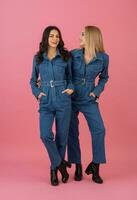 twee opgewonden aantrekkelijk meisje vrienden actief Dames poseren Aan roze achtergrond in denim algemeen hebben pret samen mode neiging foto