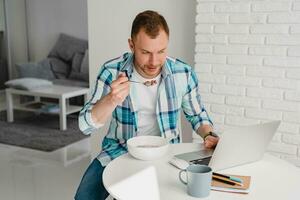 Mens in overhemd zittend in keuken Bij huis Bij tafel werken online Aan laptop foto