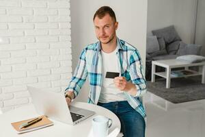 knap glimlachen Mens in overhemd zittend in keuken Bij huis Bij tafel werken online Aan laptop foto