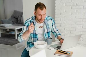 knap glimlachen Mens in overhemd zittend in keuken Bij huis Bij tafel werken online Aan laptop foto