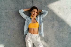 glimlachen gelukkig mooi vrouw poseren tegen beton muur Aan zonnig dag zomer mode stijl neiging foto