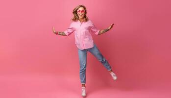 blond mooi vrouw in roze overhemd en jeans glimlachen jumping foto