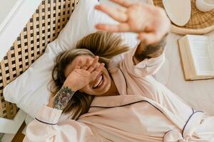 mooi glimlachen vrouw ontspannende Bij huis Aan bed in ochtend- in pyjama foto