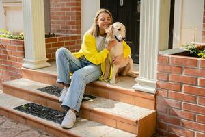 gelukkig glimlachen vrouw in geel trui wandelen Bij haar huis met een hond gouden retriever foto