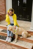 vrouw in geel trui wandelen Bij haar huis met een hond luisteren naar muziek- in hoofdtelefoons foto