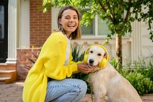 vrouw in geel trui wandelen Bij haar huis met een hond luisteren naar muziek- in hoofdtelefoons foto