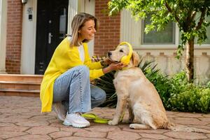 vrouw in geel trui wandelen Bij haar huis met een hond luisteren naar muziek- in hoofdtelefoons foto