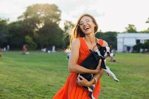 jong gelukkig glimlachen vrouw in oranje jurk hebben pret spelen met hond in park foto