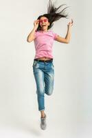 aantrekkelijk vrouw in roze t-shirt en zonnebril jumping foto