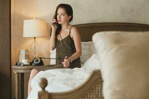 jong mooi vrouw zittend Aan bed in hotel kamer foto