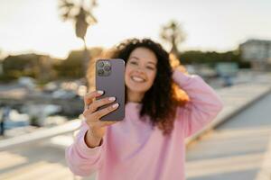 jong mooi gekruld vrouw Aan zomer vakantie met telefoon foto