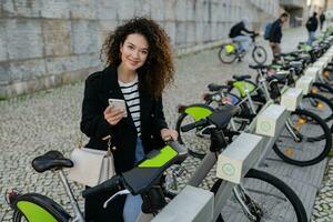 mooi gekruld vrouw huren een fiets in straat met een app foto