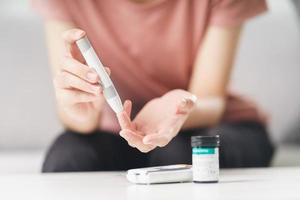 Aziatische vrouw die lancet op vinger gebruikt voor het controleren van de bloedsuikerspiegel door glucosemeter, gezondheidszorg en medisch, diabetes, glycemieconcept foto