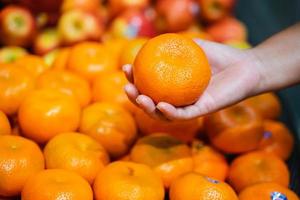 vrouwenhand die een sinaasappel kiest bij supermarkt foto