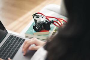 aziatische vrouw fotograaf zittend op de bank met behulp van de laptop voor werk met slr filmcamera thuis, creatief, freelance werknemersconcept. foto