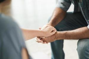 vrouwelijke vriend of familie zitten en houden elkaars hand vast tijdens het opvrolijken van de mentaal depressieve man, psycholoog biedt mentale hulp aan de patiënt. ptss geestelijke gezondheidsconcept foto