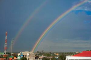 mooi veelkleurig regenboog na regen Aan blauw lucht en wit wolken in de midden- van een dorp in een gemeenschap in Thailand foto