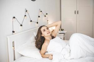 mooie jonge vrouw wakker in comfortabel bed op witte verse lakens. foto