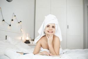 jonge gelukkige vrouw leest papieren boek in bed. foto