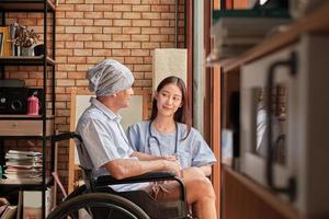 kanker oudere patiënten in rolstoelen krijgen revalidatiebehandelingen in een privéwoning, aziatische vrouwelijke artsen medische therapiebehandelingen door te praten om eenzaamheid te genezen en hen met een glimlach aan te moedigen. foto