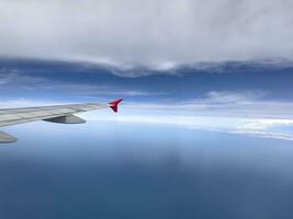 de vleugel van een modern vliegtuig vliegend in de blauw lucht met weinig wolken gedurende de reis. kopiëren ruimte naar insert tekst. foto